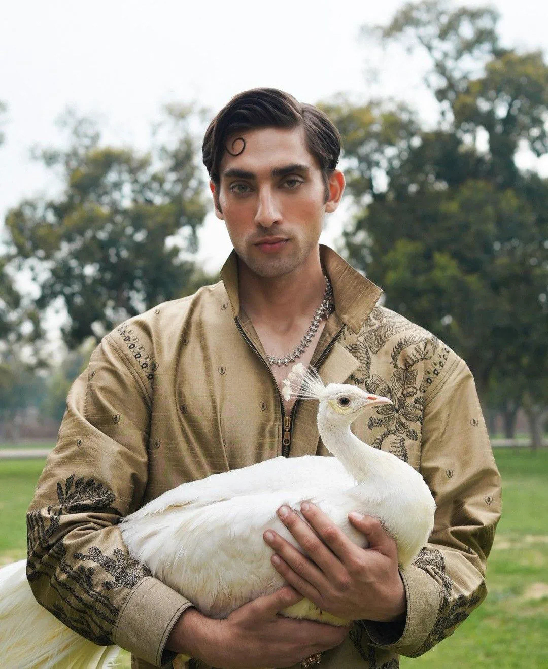Man in an embroidered kurta holding a white peacock