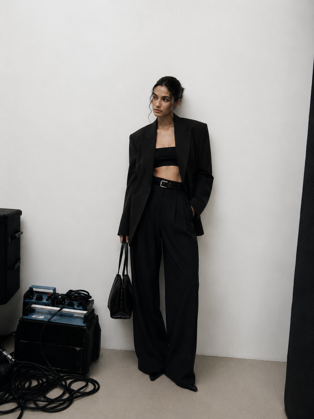 Woman in a black suit holding a leather bag on set