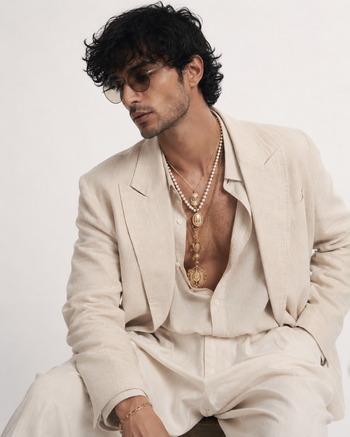 Man in a cream linen suit layered with pearl necklaces
