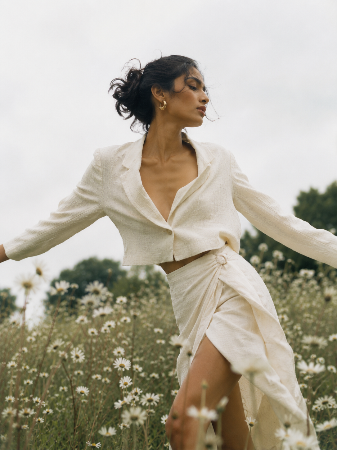 Woman in a cream linen co-ord turning through a daisy field